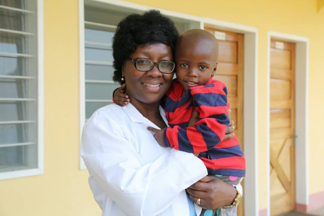 A woman in a medical coat is smiling while holding a child