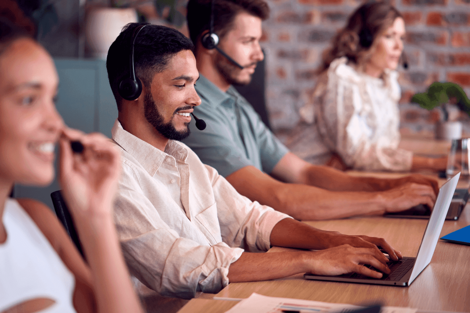 A group of customer support professionals wearing headsets and working on laptops in an office environment.