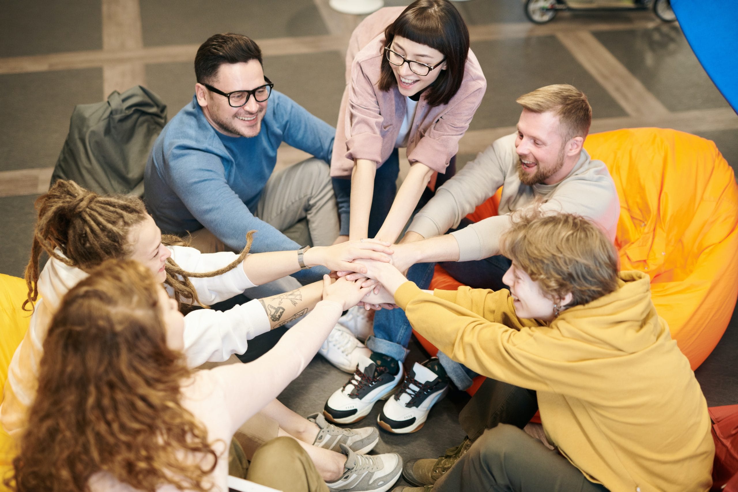 A group of young adults are sitting in a circle with their hands stacked together