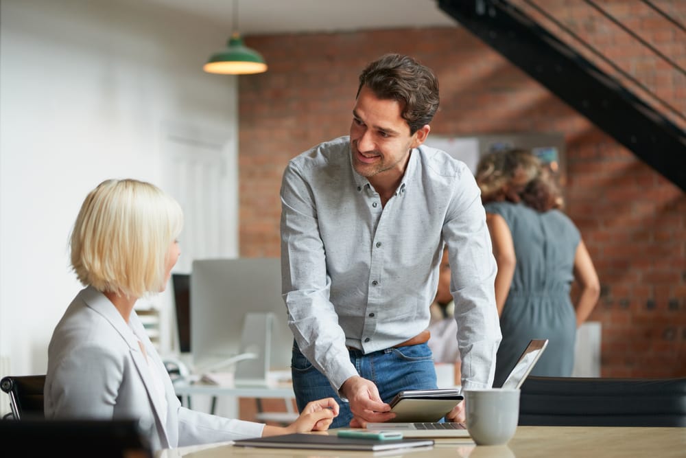 A man and a woman are talking near a table in a large modern office