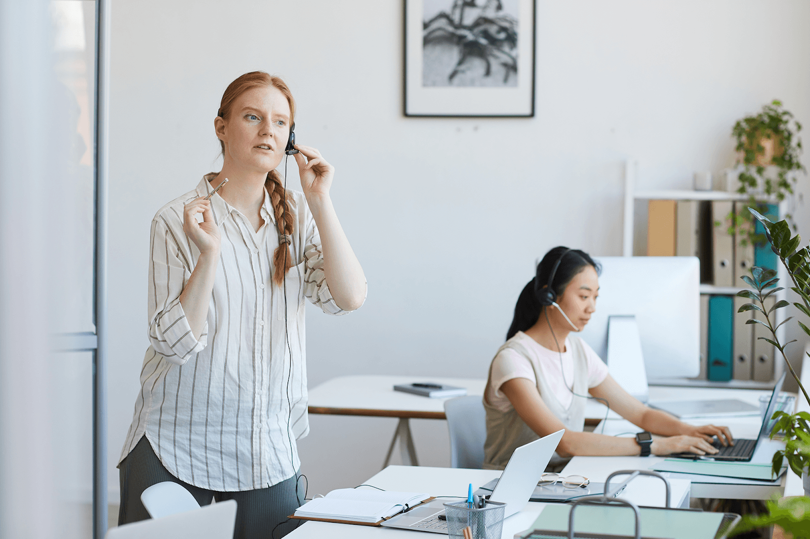 Two women working in an office, one wearing a headset.