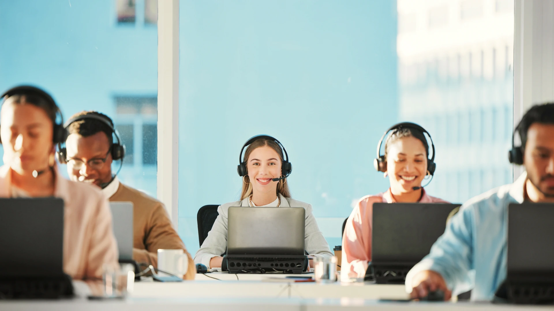 Smiling customer support representatives wearing headsets and working at their computers.