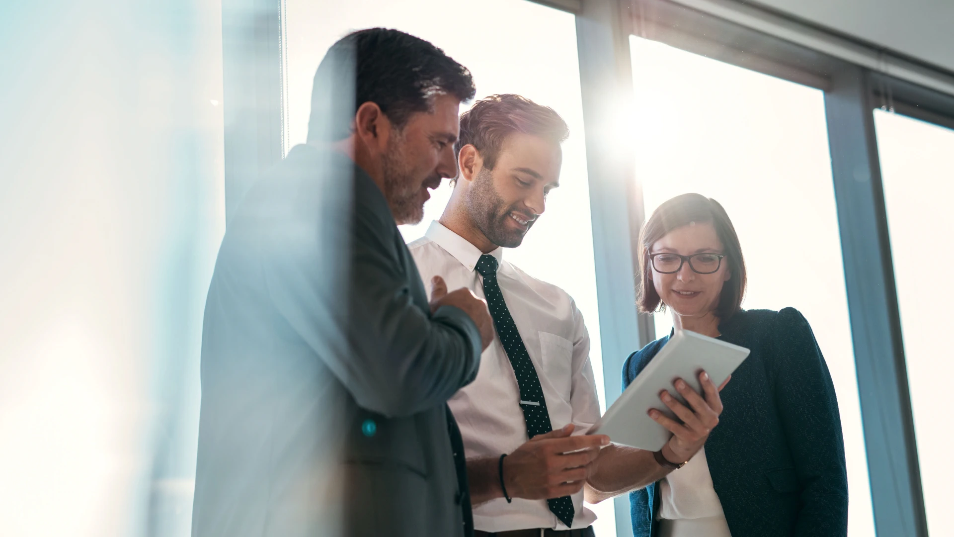 Three business professionals collaborating and reviewing information on a tablet.