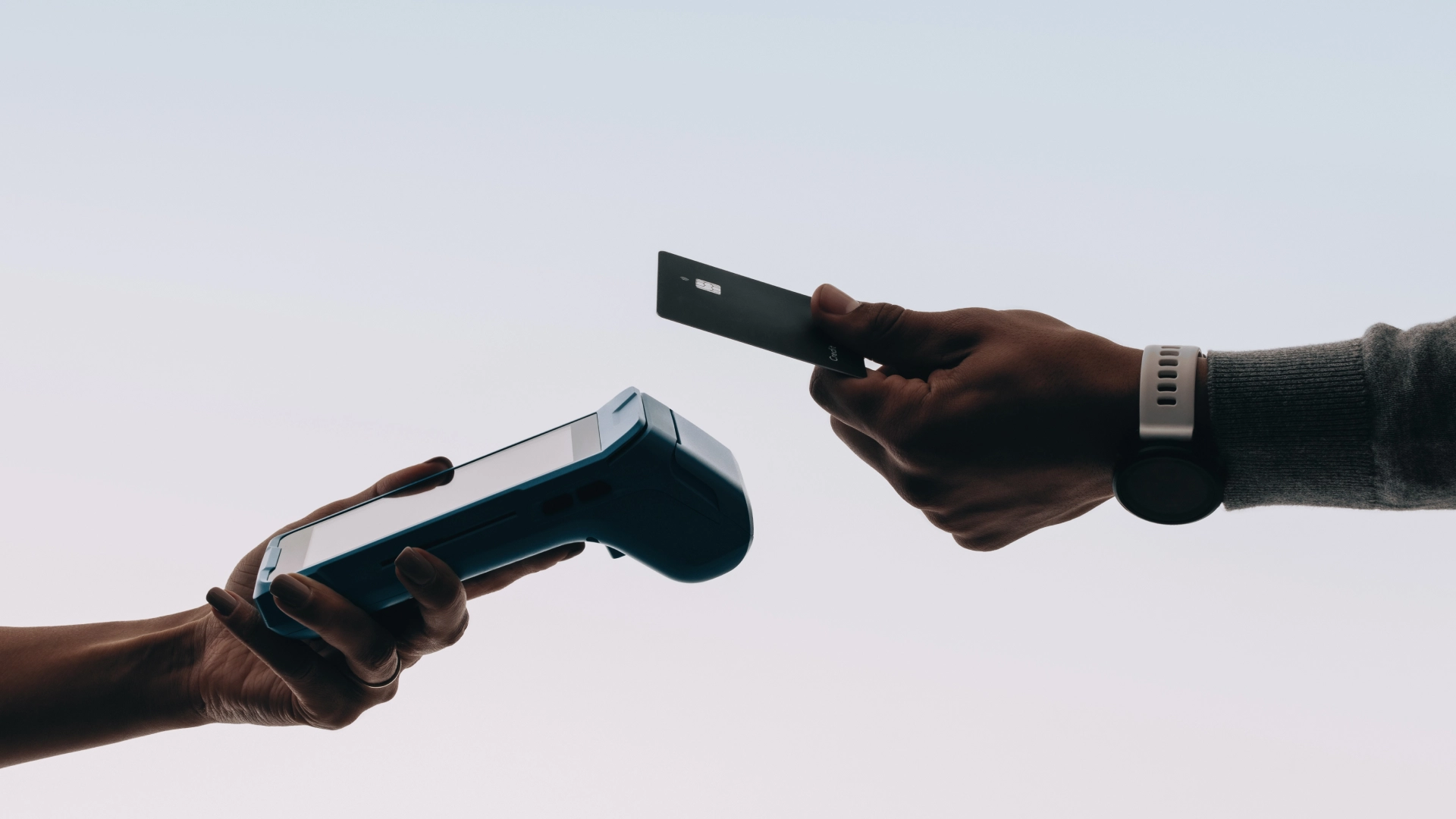 Hands holding a credit card and a payment terminal for a contactless transaction.