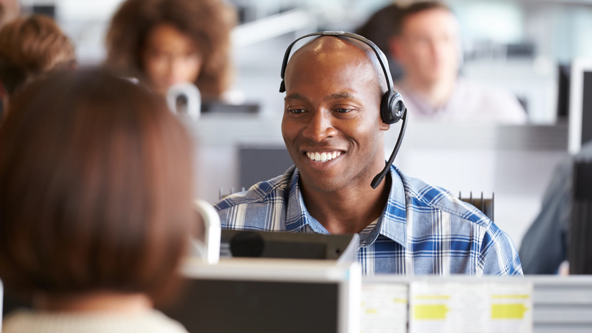 Smiling customer service representative wearing a headset at his workstation.