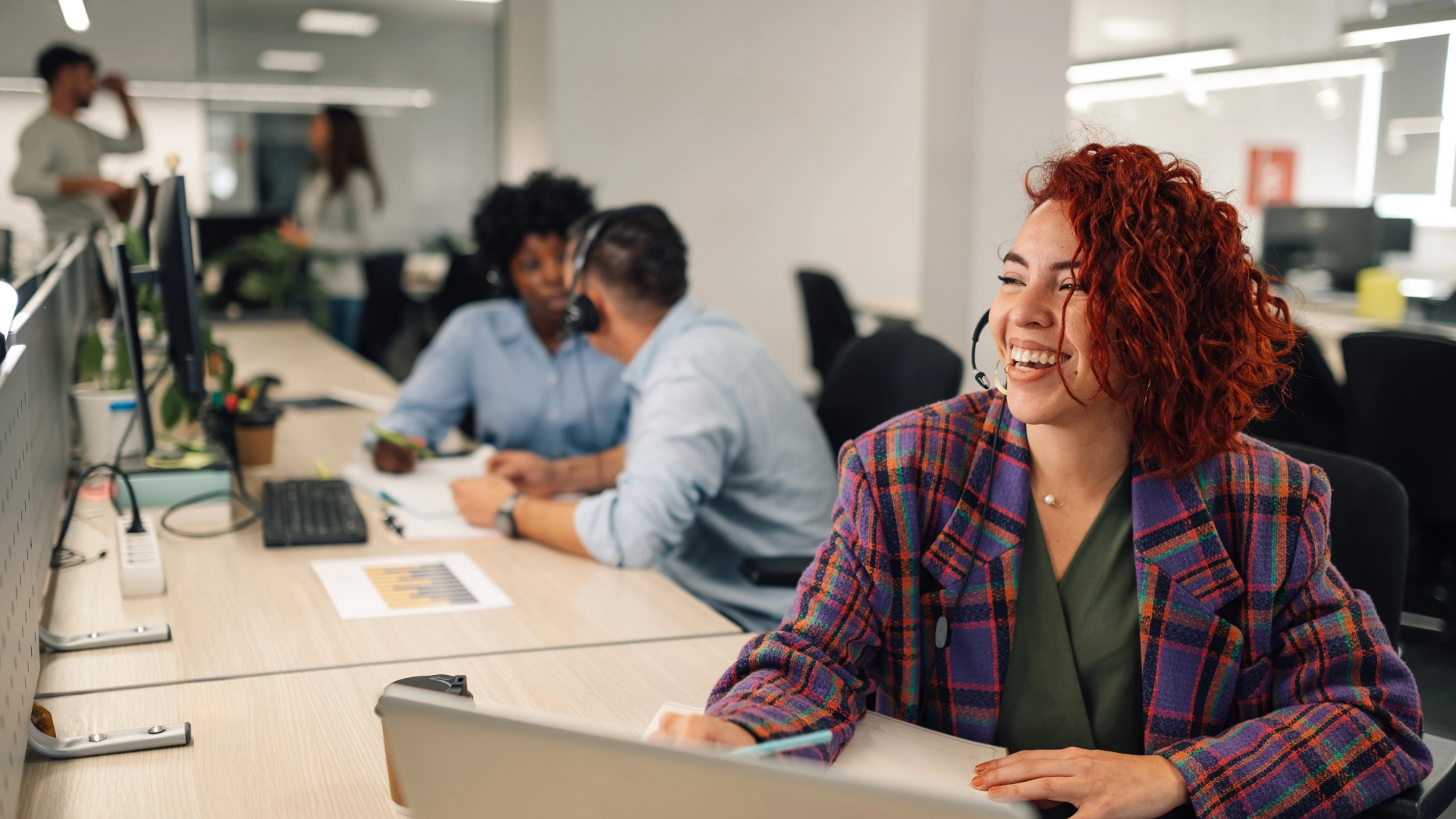 Smiling customer support agent with headset in a vibrant, collaborative office.