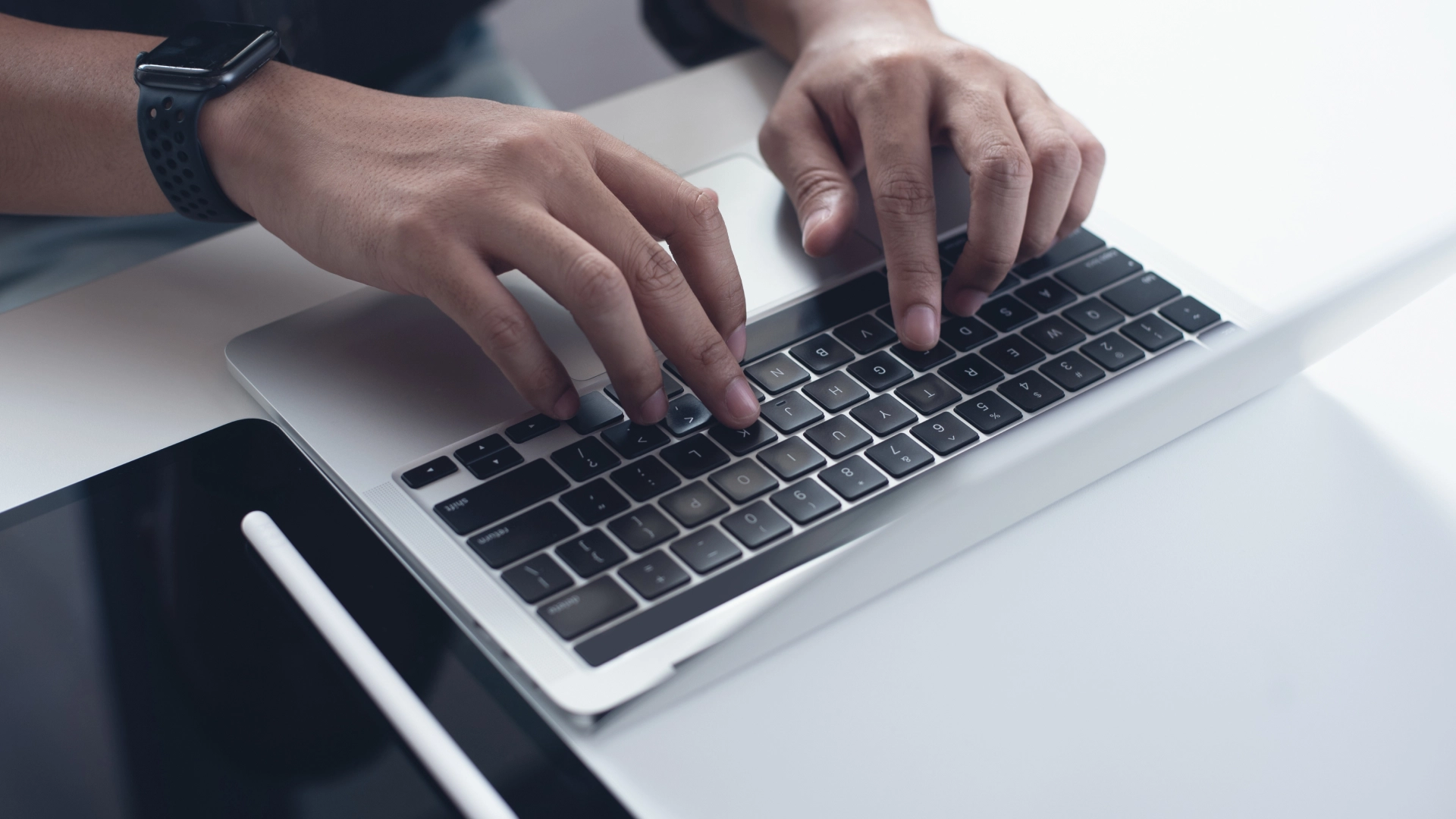 Person working on a laptop, with a tablet and stylus nearby.