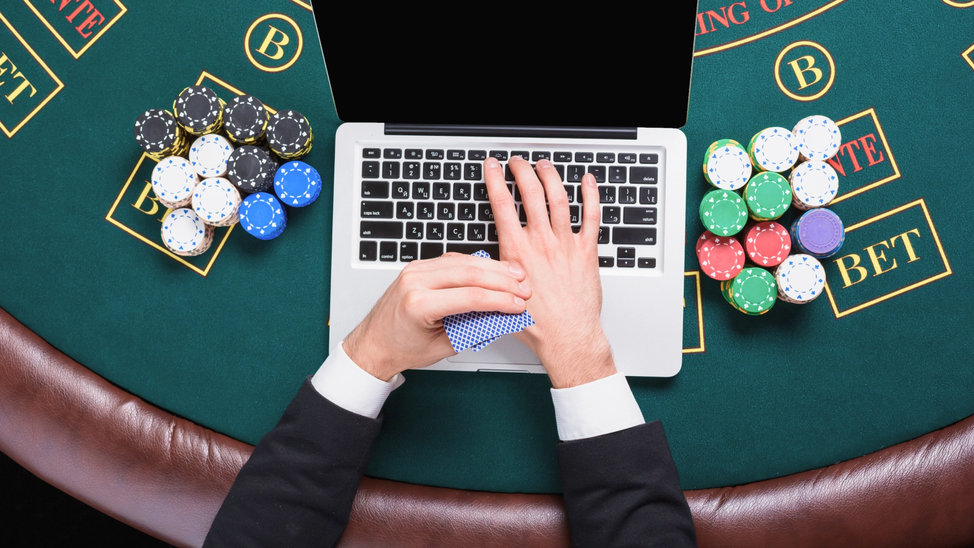 Man engaged in a poker game with a laptop on the table.