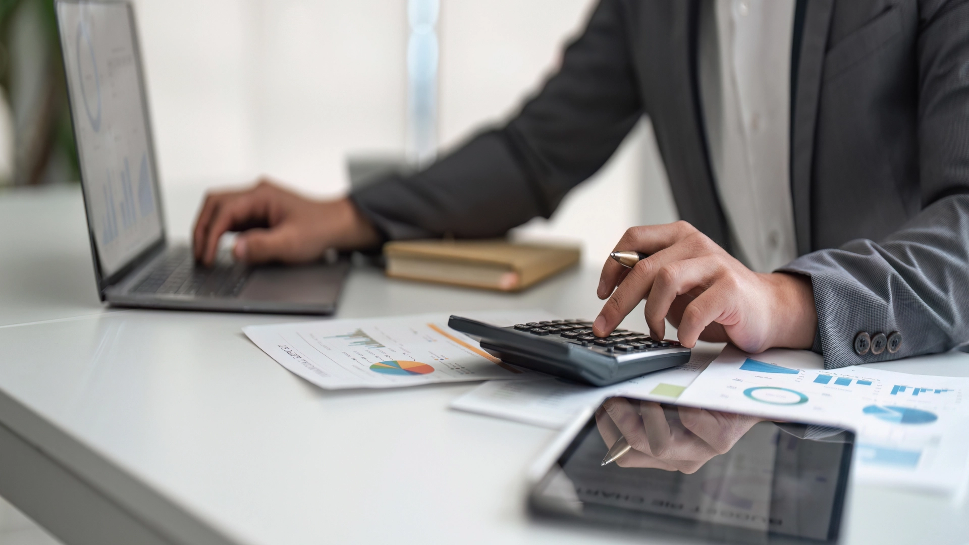 Man calculating financial data with a calculator and laptop.