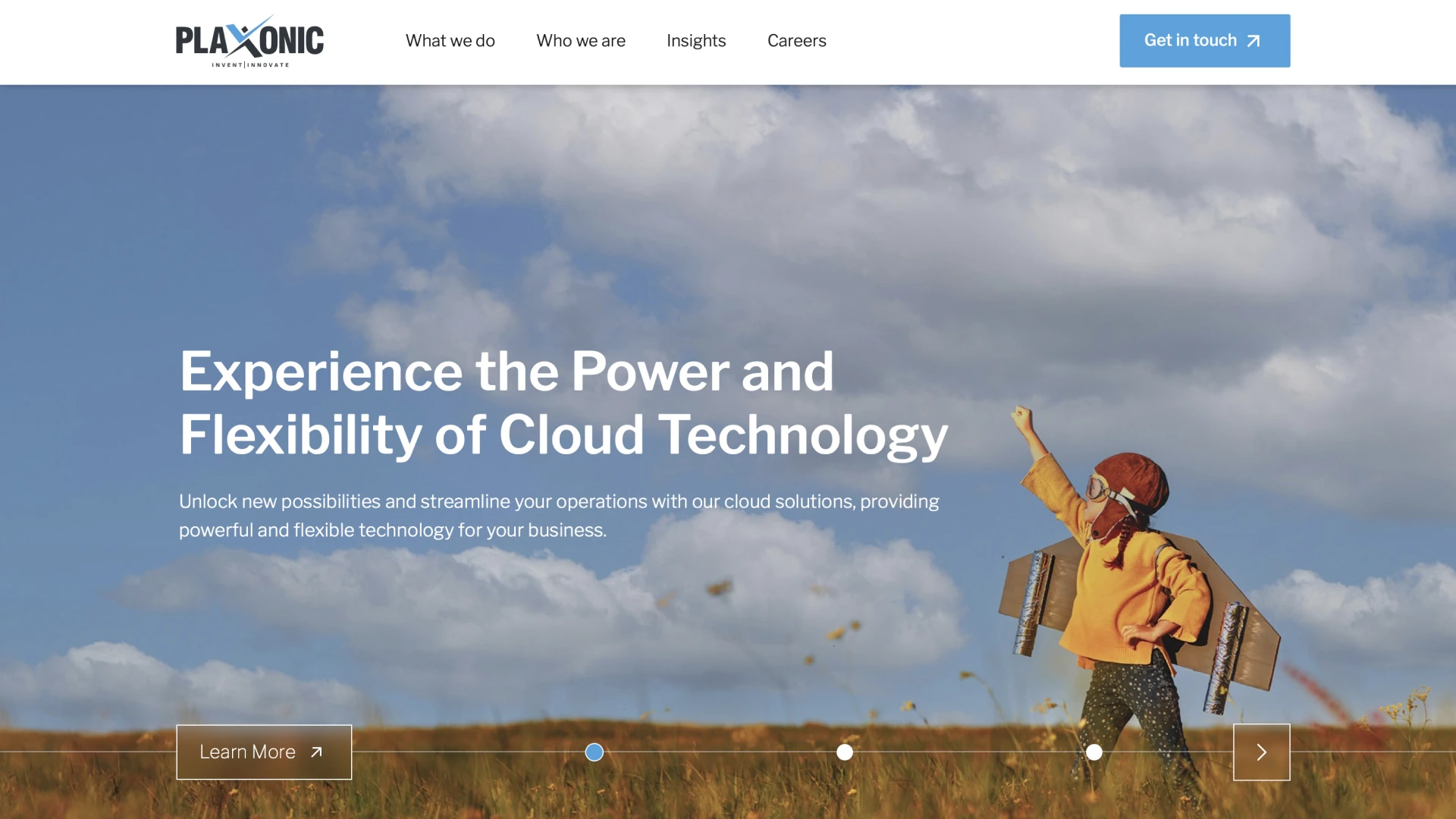 Plaxonic homepage features the tagline 'Experience the Power of Flexibility of Cloud Technology,' with a blue sky and clouds in the background, and a glade where a boy in aviator goggles stands with cardboard wings on his back.